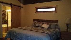 Un dormitorio con una cama grande, cabecera de madera, un ventanal pequeño y una puerta que da al baño.