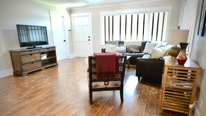 Un salon doté d’un parquet, d’un téléviseur posé sur un meuble en bois, d’un canapé, d’un fauteuil et d’une lampe.