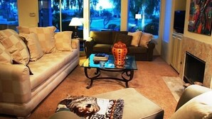 A living room with a beige sofa, a glass coffee table, and a fireplace. - Pond View Villa @ Desert Princess Country Club & Golf Resort (Cathedral City)