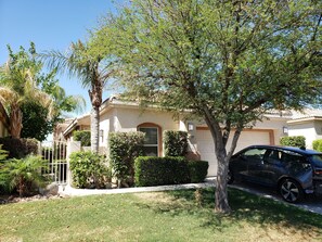 Stucco house with a flat roof, surrounded by a well-manicured lawn and lush greenery.