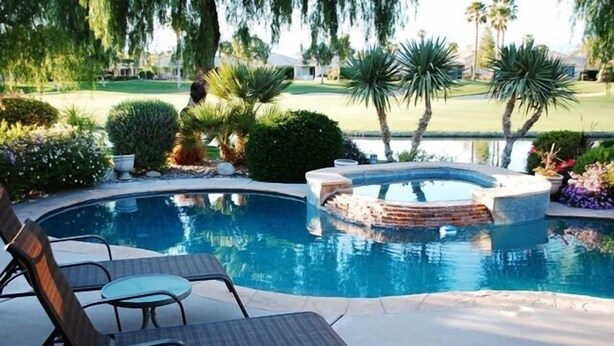 A swimming pool with lounge chairs, surrounded by landscaped greenery and a view of a golf course. - Pond View Villa @ Desert Princess Country Club & Golf Resort (Cathedral City)