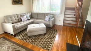 A living room with a sectional sofa, a patterned rug, a staircase, and a painting on the wall. - Sea La Vie: Ocean Side North End 3-Bedroom  - 2 min Walk to Beach (Virginia Beach)