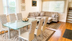 A dining area with a glass table and chairs, a sofa, and a staircase. - Sea La Vie: Ocean Side North End 3-Bedroom  - 2 min Walk to Beach (Virginia Beach)