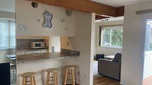 A modern kitchen with wooden stools, a microwave, and a unique wall clock. - Sea La Vie: Ocean Side North End 3-Bedroom  - 2 min Walk to Beach (Virginia Beach)
