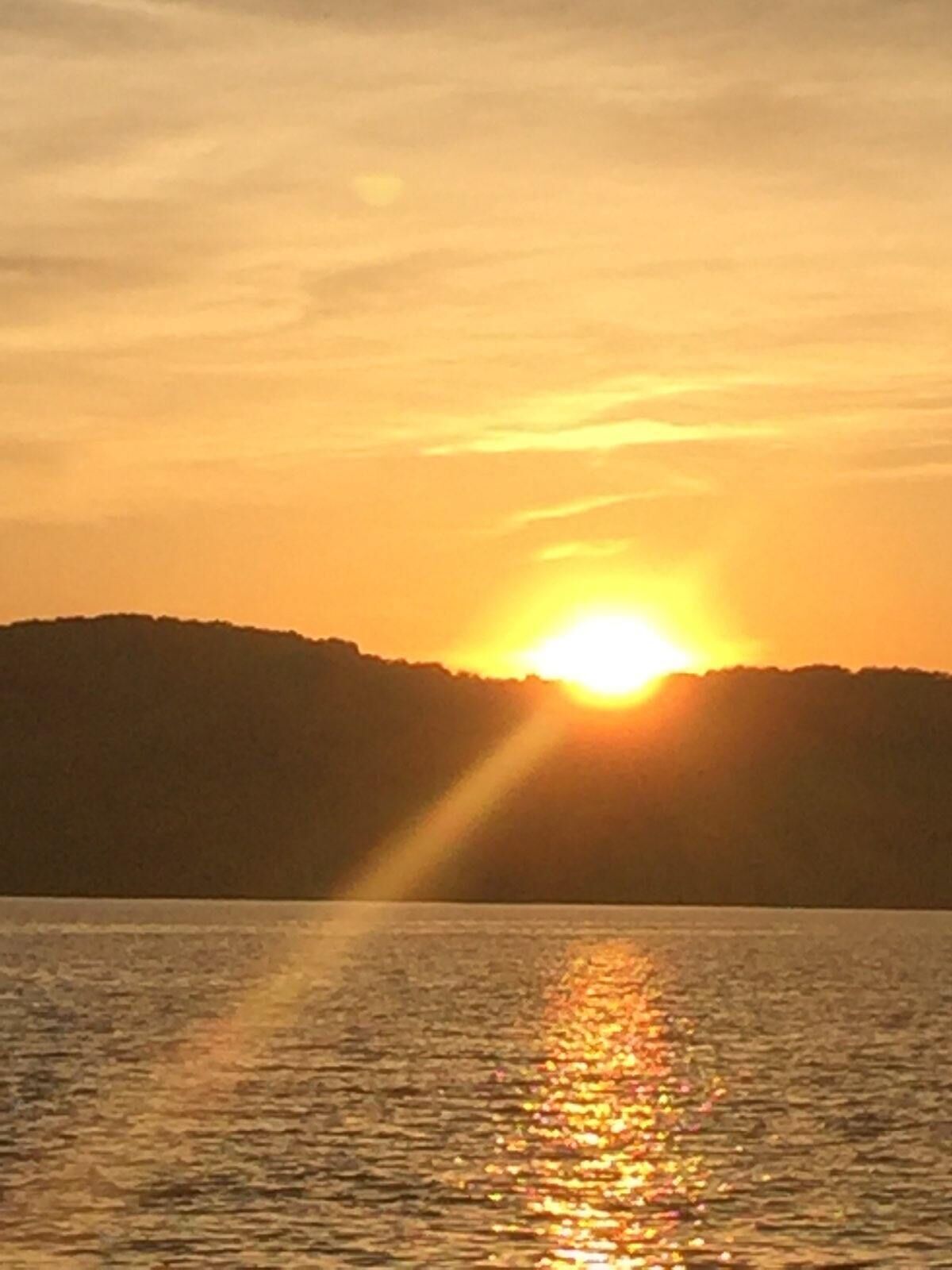 Un coucher de soleil sur une étendue d’eau, avec la silhouette d’une colline en arrière-plan.