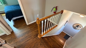 A staircase with wooden railings, a fire extinguisher, and a bed in the background.