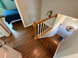 A staircase with wooden railings, a fire extinguisher, and a bed in the background.