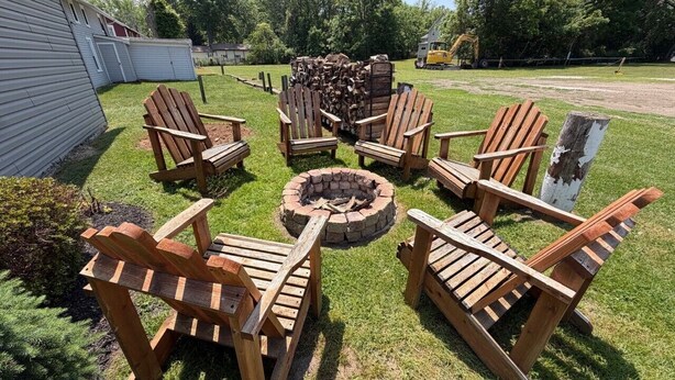 A backyard with a fire pit, wooden chairs, and a stack of firewood.