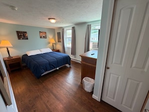 A bedroom with a bed, bedside lamps, a desk, and a window.