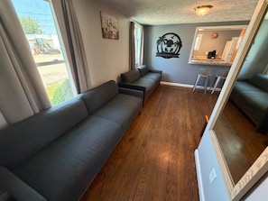A living room with a sofa, a dining area with a bar, and a kitchen visible through an open doorway.