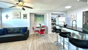 Ein modernes Wohnzimmer mit einem dunkelgrauen Sofa, einem Deckenventilator und einem Essbereich mit roten Stühlen.