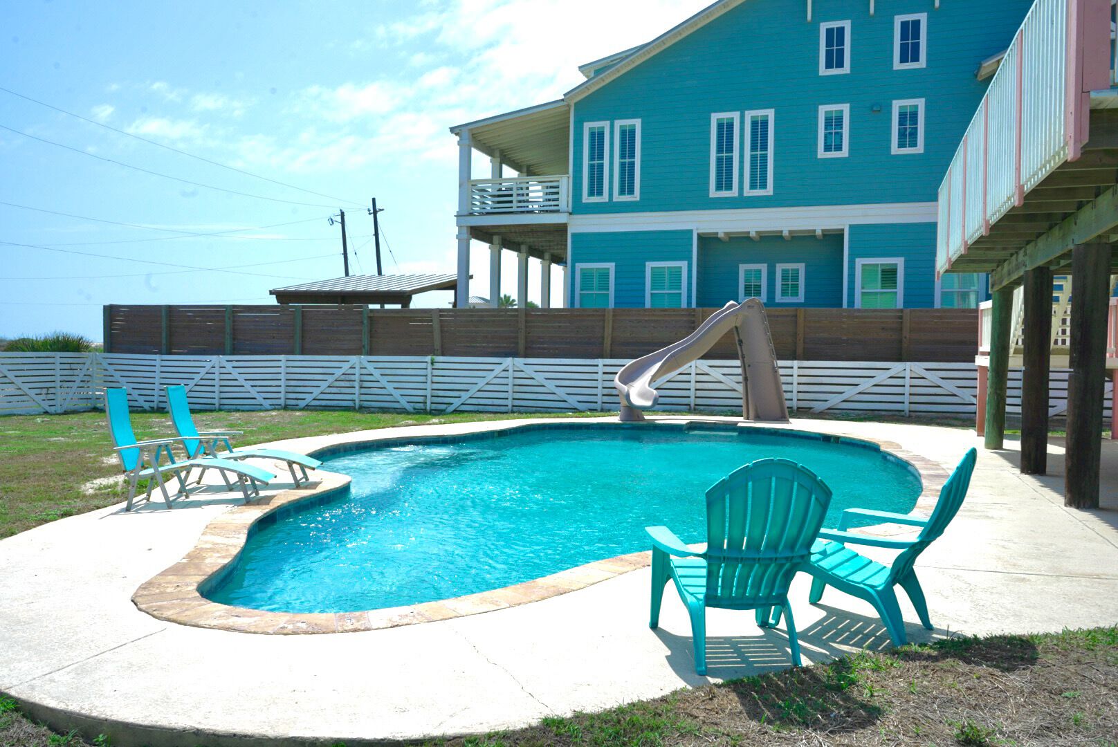 Une piscine avec un toboggan, deux chaises et un bâtiment en arrière-plan.