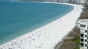 Une plage avec une rive de sable blanc, une mer d’un bleu limpide et, en arrière-plan, une rangée d’immeubles de grande hauteur.