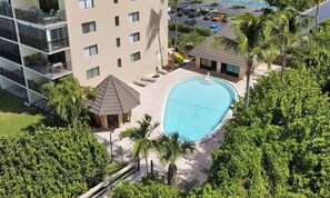 A hotel with a swimming pool surrounded by palm trees and a parking lot.