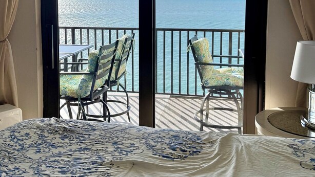 Une chambre d’hôtel avec un grand lit et deux fauteuils placés face à un balcon donnant sur la mer.