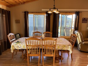 Uma sala de jantar com mesa e cadeiras de madeira, um lustre e janelas amplas com cortinas.