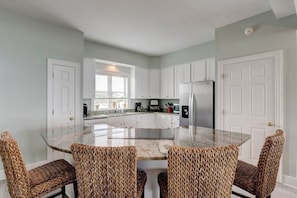 A modern kitchen with white cabinets, a central island, and woven chairs.