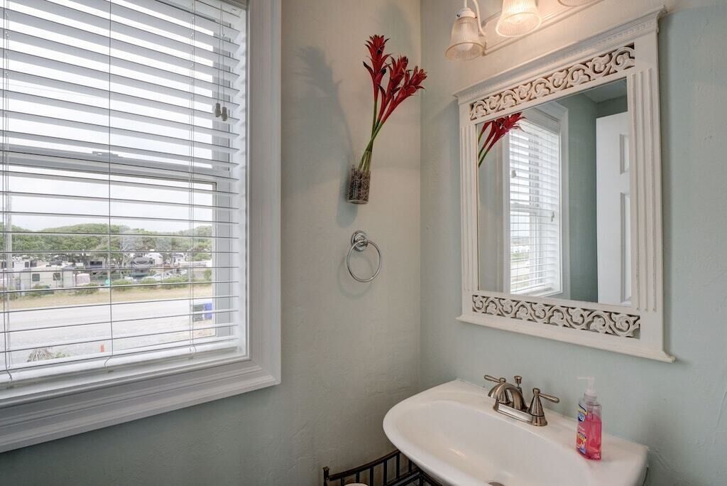 A bathroom with a white sink, a mirror with decorative molding, and a window with blinds.