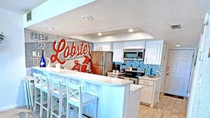 A modern kitchen with a central island, white cabinetry, and a lobster-themed sign.