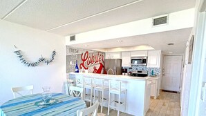A modern kitchen with white cabinetry, a central island, and a dining area with a blue-striped tablecloth.