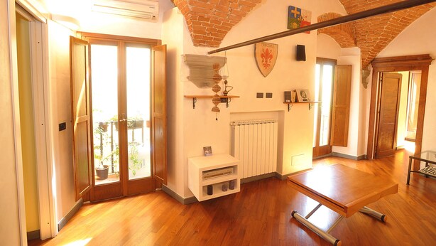 Una habitació àmplia amb terra de fusta, un radiador i un sostre amb maó a la vista.