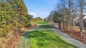 A golf course with a clear path, surrounded by trees and a sidewalk.