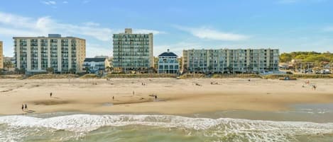 Un hotel frente a la playa con varias construcciones, arena y olas del océano.