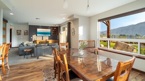 A spacious living room with a large wooden dining table, comfortable seating, a TV, and a scenic view through a large window. - Incredible Views of Lake Chelan-Pool, Outdoor Spas (Manson)