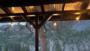 A covered outdoor seating area with a view of a wooded landscape and a lake.