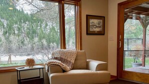 A cozy living room with a beige armchair, a small side table, and a large window offering a view of a snowy landscape.