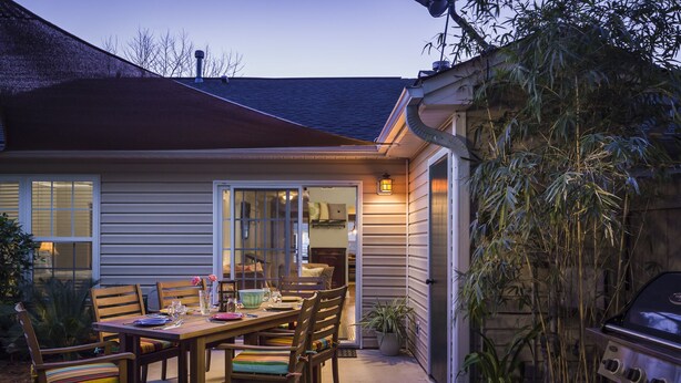 A patio with a dining table and chairs, a grill, and a potted plant.