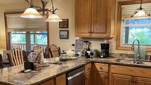 A kitchen with wooden cabinets, granite countertops, a dishwasher, and a window with blinds. - Escape and Heal your body and soul (Sparta)