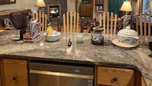 A kitchen with granite countertops, a stainless steel dishwasher, wooden cabinets, a stone fireplace, and a deer antler chandelier. - Escape and Heal your body and soul (Sparta)