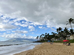 Une plage bordée de palmiers, un parasol rouge et une montagne en arrière-plan.