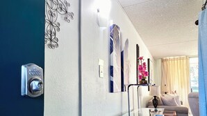 Habitación de hotel moderna con separador de vidrio, cerradura electrónica, sofá, una mesita pequeña y decoración en la pared.