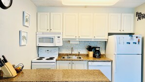 Una cocina con gabinetes blancos, microondas, estufa, fregadero y refrigerador.