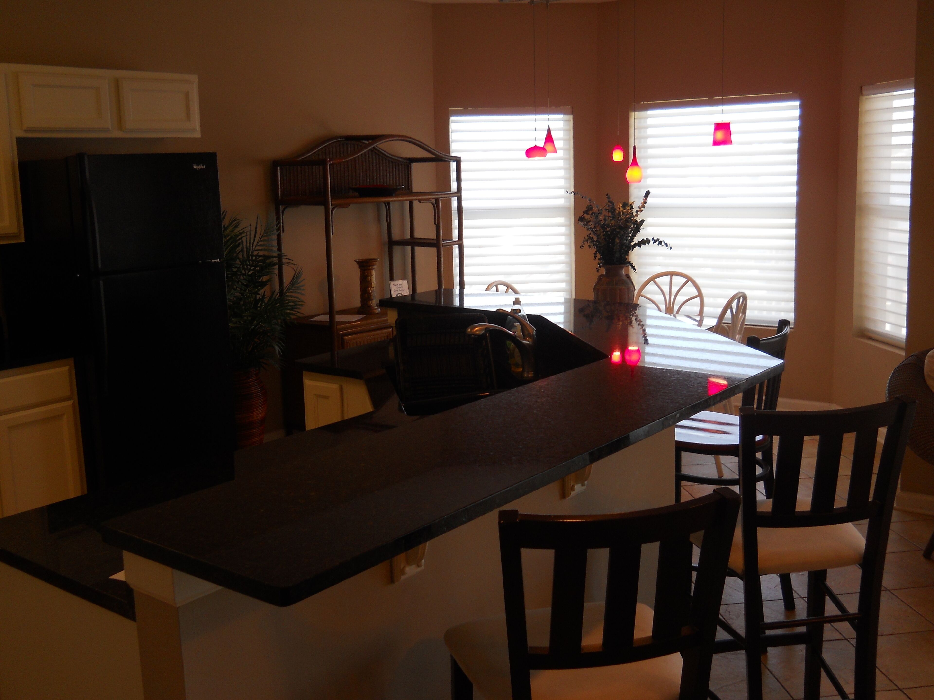 A kitchen with a dark countertop, wooden chairs, a dining table, and a black refrigerator.