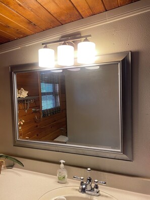 A bathroom with a large mirror, wooden ceiling, and a white sink with a soap dispenser.