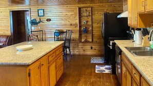 Interior de una cabaña de madera con cocina, que cuenta con encimeras de granito, armarios de madera y un refrigerador negro.
