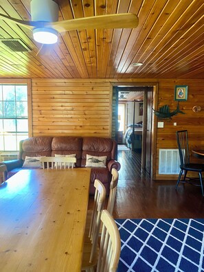 A wooden interior with a dining table, chairs, a leather sofa, and a ceiling fan.