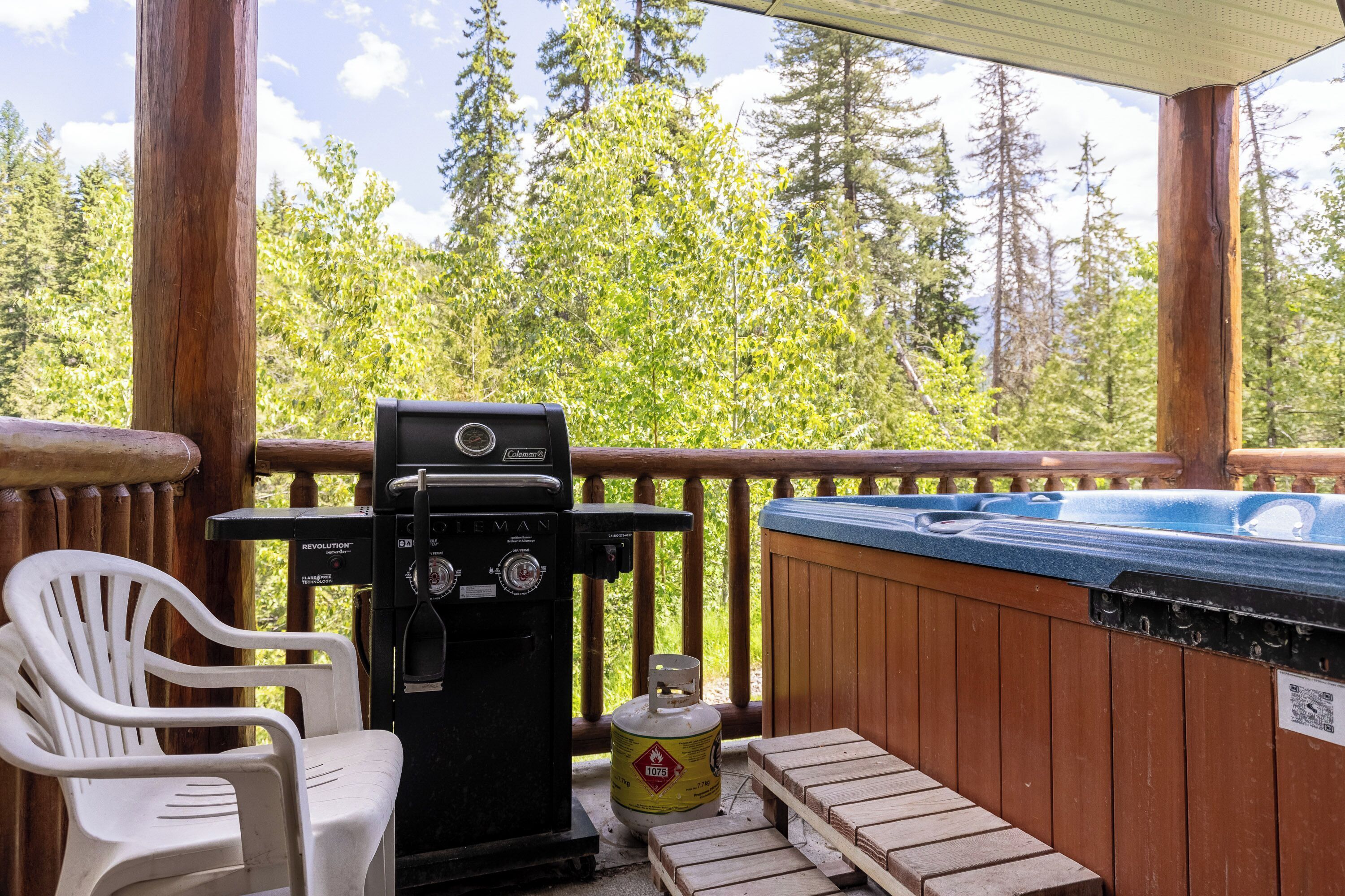 A wooden deck with a hot tub, a Coleman grill, and a white plastic chair.