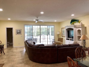 A living room with a large sectional sofa, a glass dining table, and a TV on a white entertainment unit.
