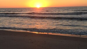A beach with waves and a setting sun.