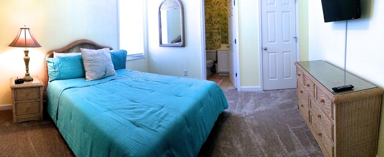 A bedroom with a bed, a nightstand, a dresser, a television, and a mirror.