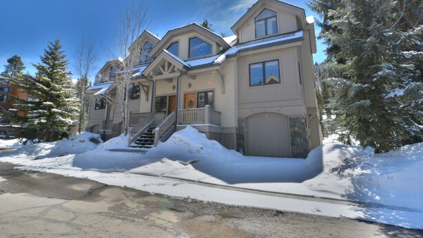 Una casa grande de varios pisos con una escalera principal destacada, paisajes nevados y un cielo azul despejado.