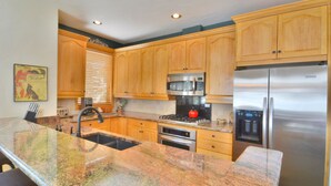 Una cocina con armarios de madera, un refrigerador de acero inoxidable, un microondas, un horno y una encimera de granito.