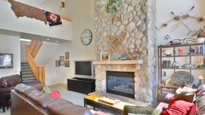 Una sala de estar con chimenea de piedra, sofás de cuero, televisión y una estantería.