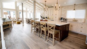 A spacious kitchen with a large island, wooden chairs, and pendant lighting.