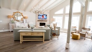 A spacious living room with a large sofa, a wooden coffee table, and a television mounted above a fireplace.