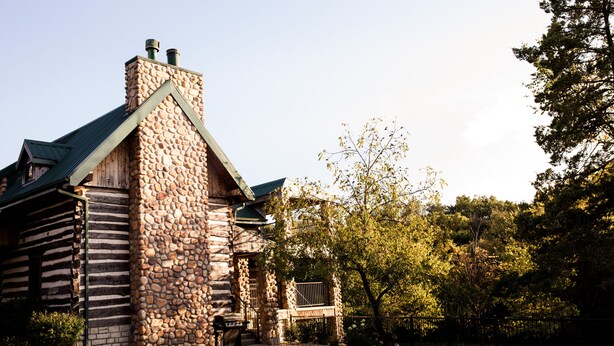 A log cabin with a stone chimney, a porch, and a fenced yard. - Beautiful secluded Log Home - Nestled in the country! (Wright City)
